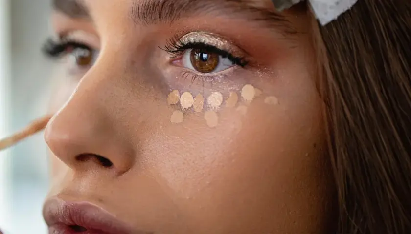 Kleine Tupfer von hellem Concealer unter dem Auge, um zu zeigen, was ein Concealer ist und wie er kleine Makel abdeckt.
