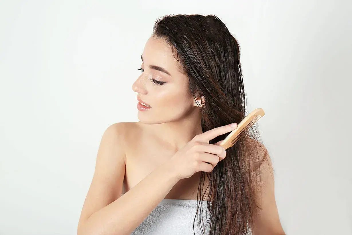 Junge Frau kämmt nasses Haar mit einem Holzkamm. Sie achtet auf ihre Spitzen, um abgebrochene Haare zu vermeiden.