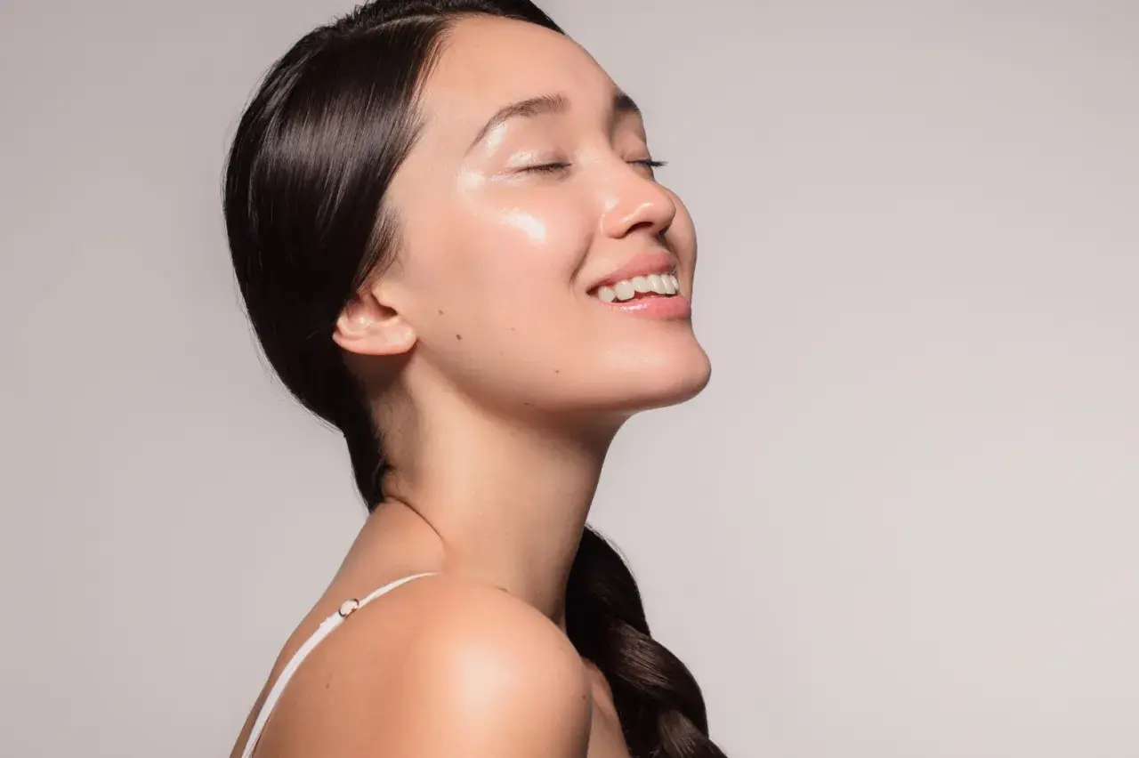 Ein lächelndes Gesicht mit strahlender, **glass skin**-ähnlicher Haut, die von Feuchtigkeit glänzt.