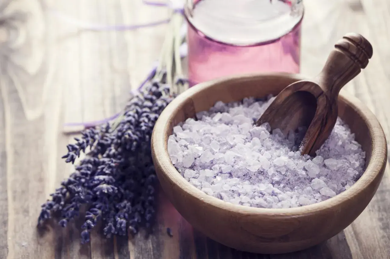 Lavendel und Kristallsalz in einer Holzschale, ideal zum badesalz selber machen. Daneben eine kleine Flasche mit lila Flüssigkeit.