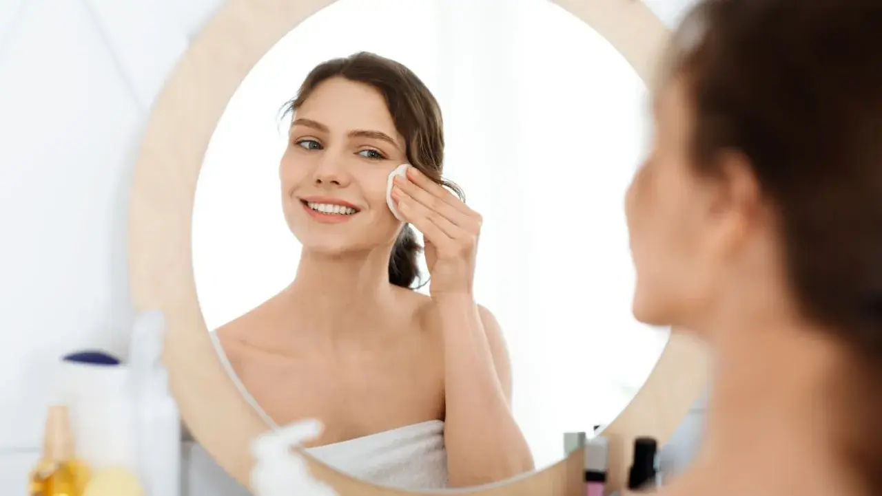 Lächelnde Frau reinigt ihr Gesicht mit einem Wattepad. Sie nutzt die Kraft von Retinol gegen Akne für reine Haut.