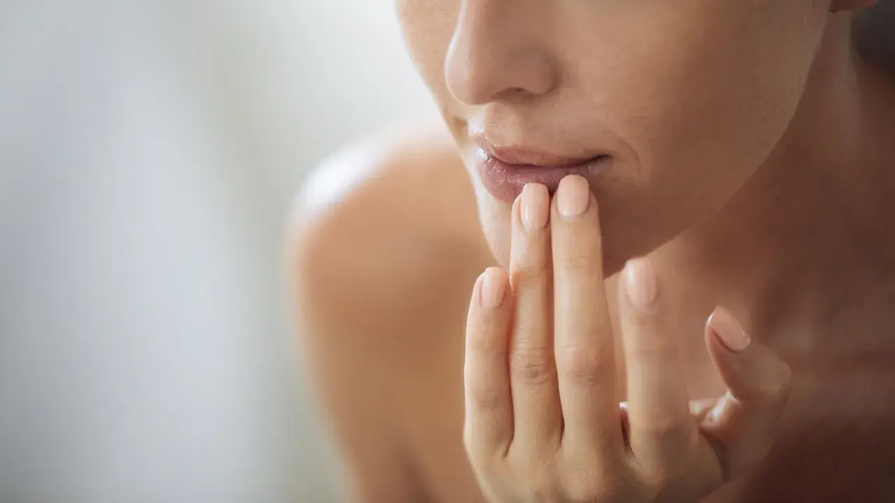 Frau trägt Lippenbalsam auf, um trockene Lippen zu behandeln. Sanfte Pflege für geschmeidige Lippen.