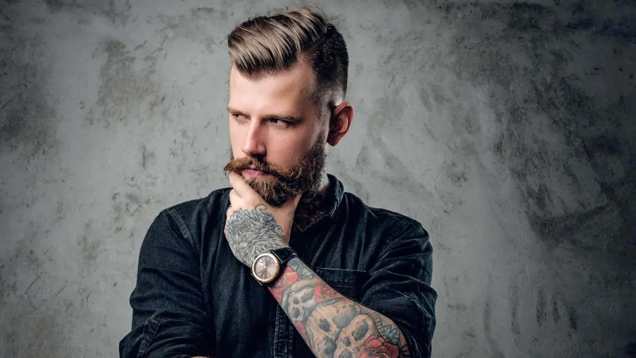 Ein Mann mit Bart und Tattoos, dessen Frisur mit Pomade gestylt ist. Er denkt nach, was ist Pomade?