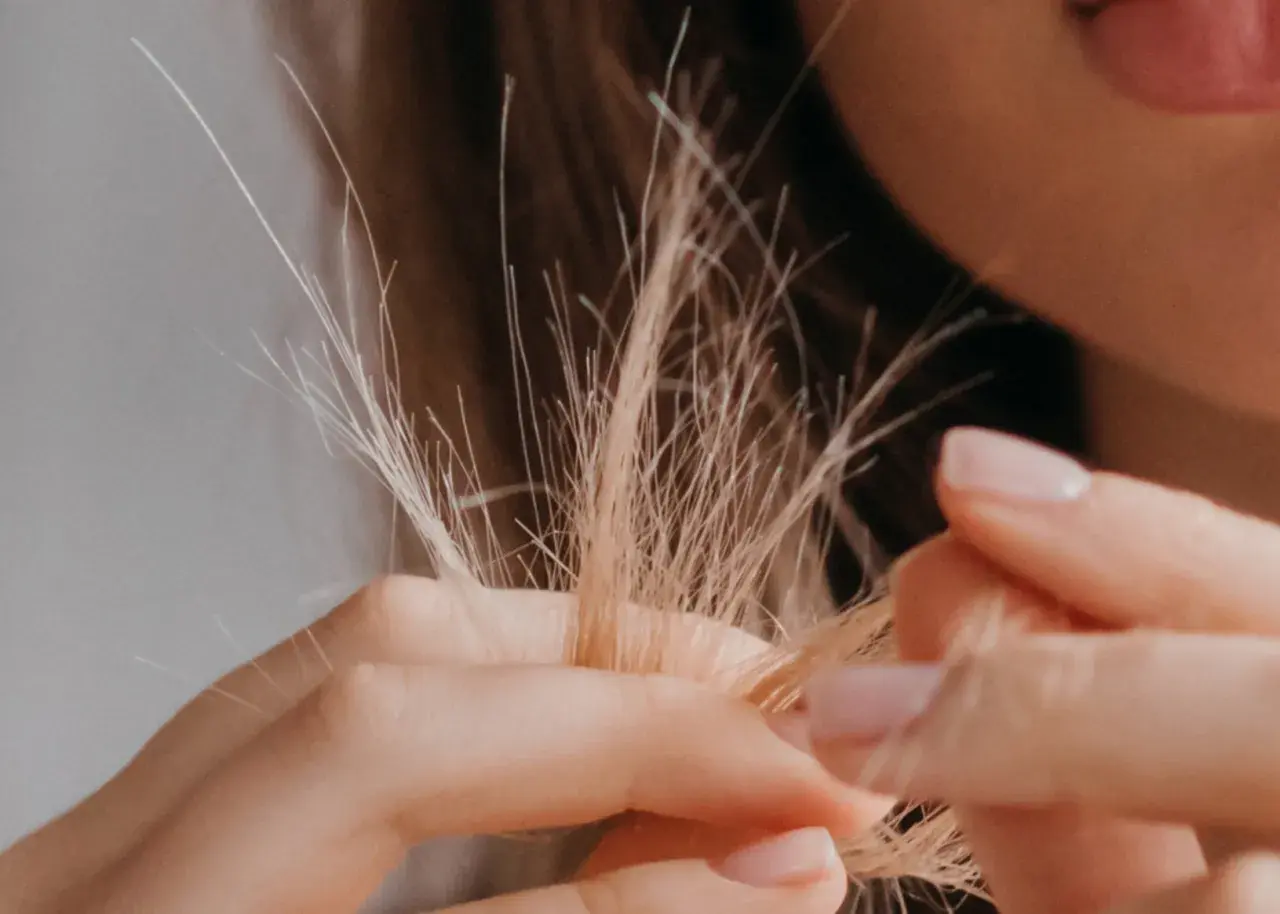 Nahaufnahme von blondem Haar, das sich in den Fingern verheddert. Die feinen, abstehenden Härchen zeigen, wie sieht Frizz aus.