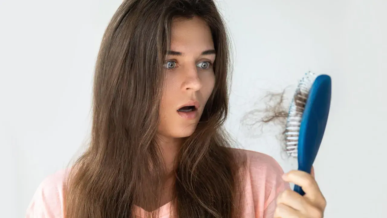 Schockiert blickt eine Frau auf ihre Haarbürste mit vielen ausgefallenen Haaren. Hoffentlich hilft Rosmarin Haare vorher nachher.