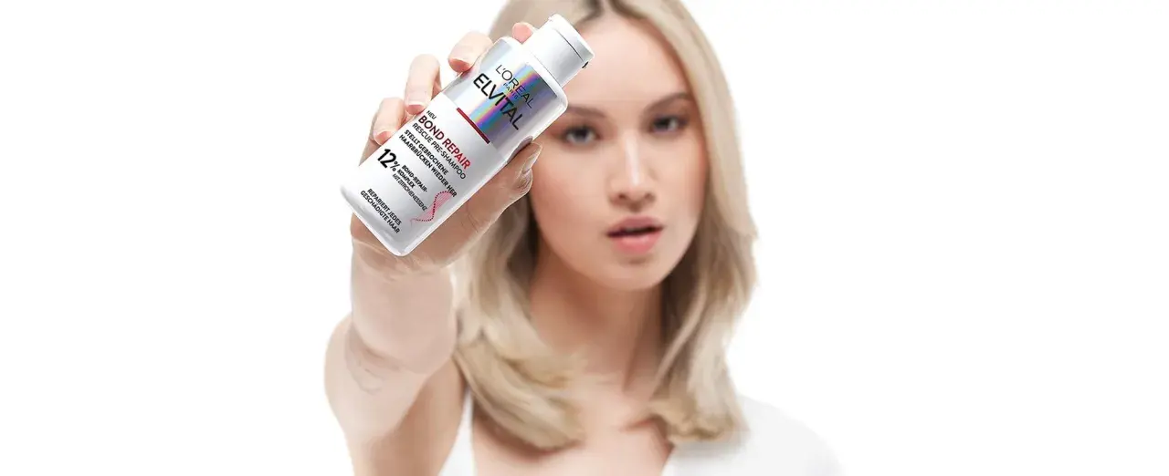 Frau hält L'Oréal Elvital Bond Repair Pre-Shampoo, das hilft, trockene Haare zu reparieren.