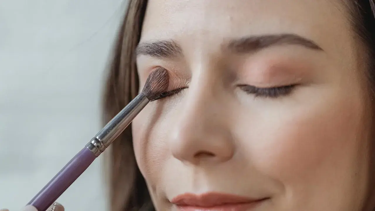 Eine Frau trägt mit einem Pinsel sanft Lidschatten auf. So gelingt das lidschatten richtig auftragen für einen strahlenden Blick.
