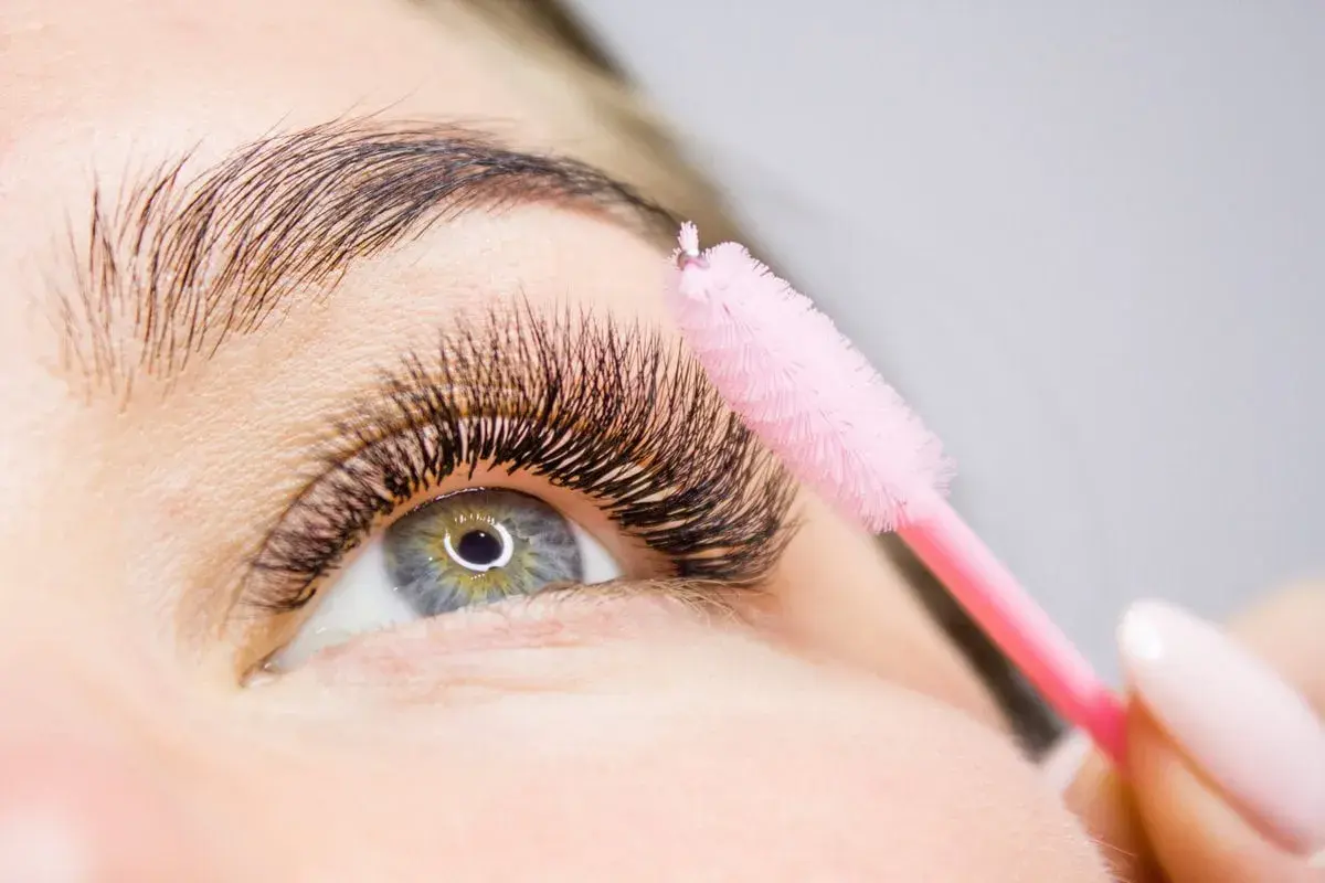Ein rosa Bürstchen wird sanft über voluminöse Wimpern geführt, um die **Wimpern pflegen** und perfekt zu stylen.