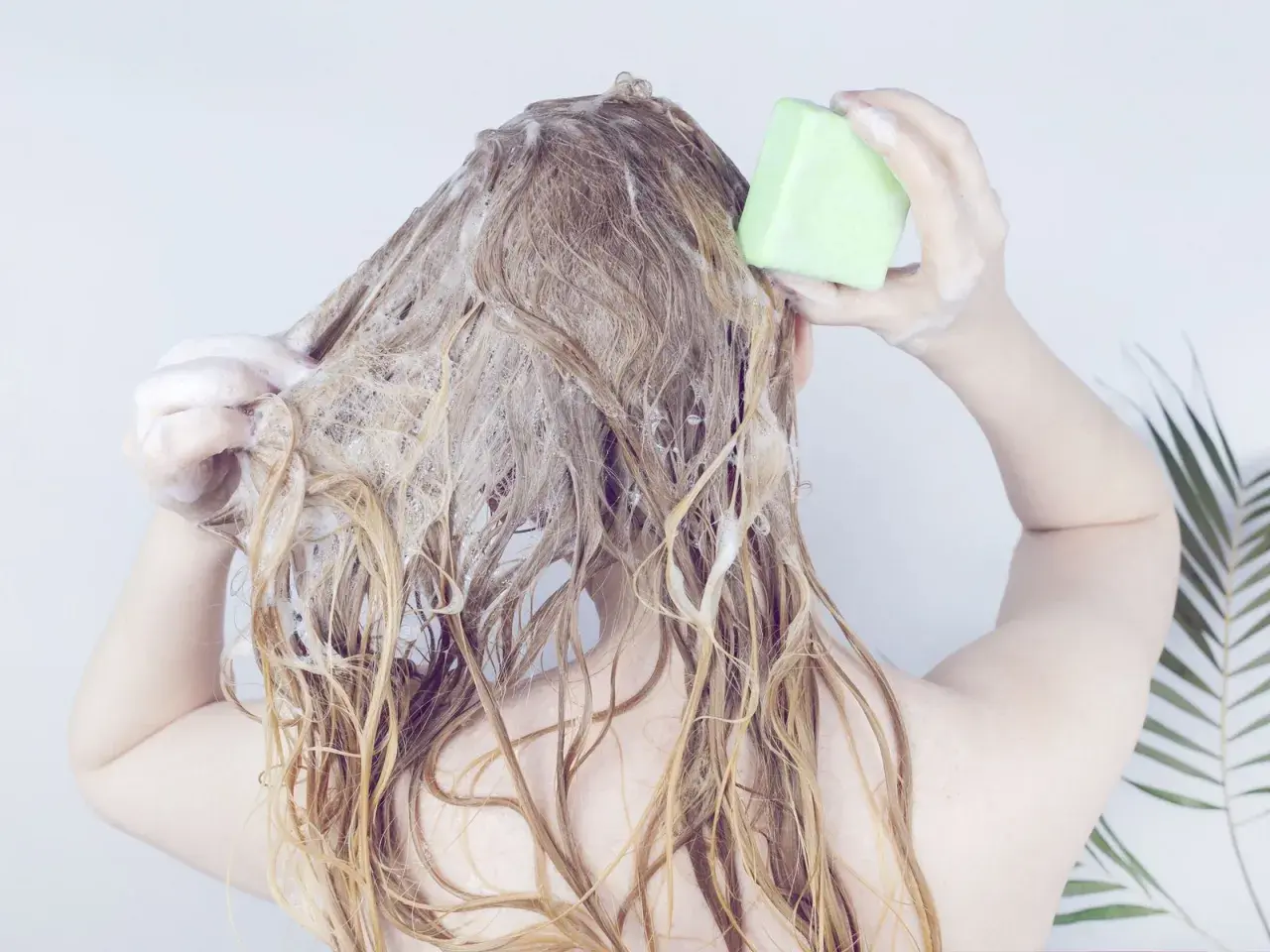 Frau wäscht sich die Haare mit einem grünen Stück biologisch abbaubares Shampoo.
