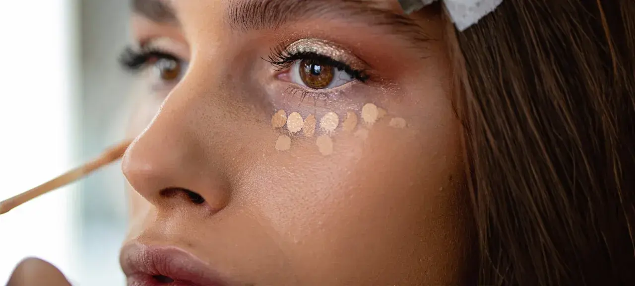 Kleine Tupfer von hellem Concealer unter dem Auge, um zu zeigen, was ein Concealer ist und wie er kleine Makel abdeckt.