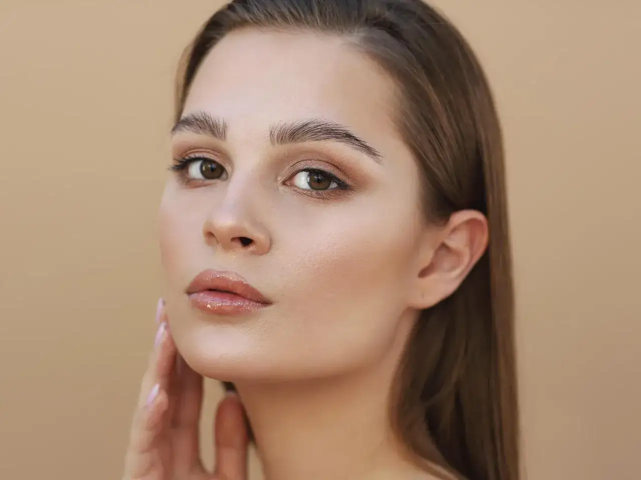 Ein dezentes Augen Make-up betont die braunen Augen einer jungen Frau. Ihre Lippen sind mit einem glänzenden Gloss veredelt.