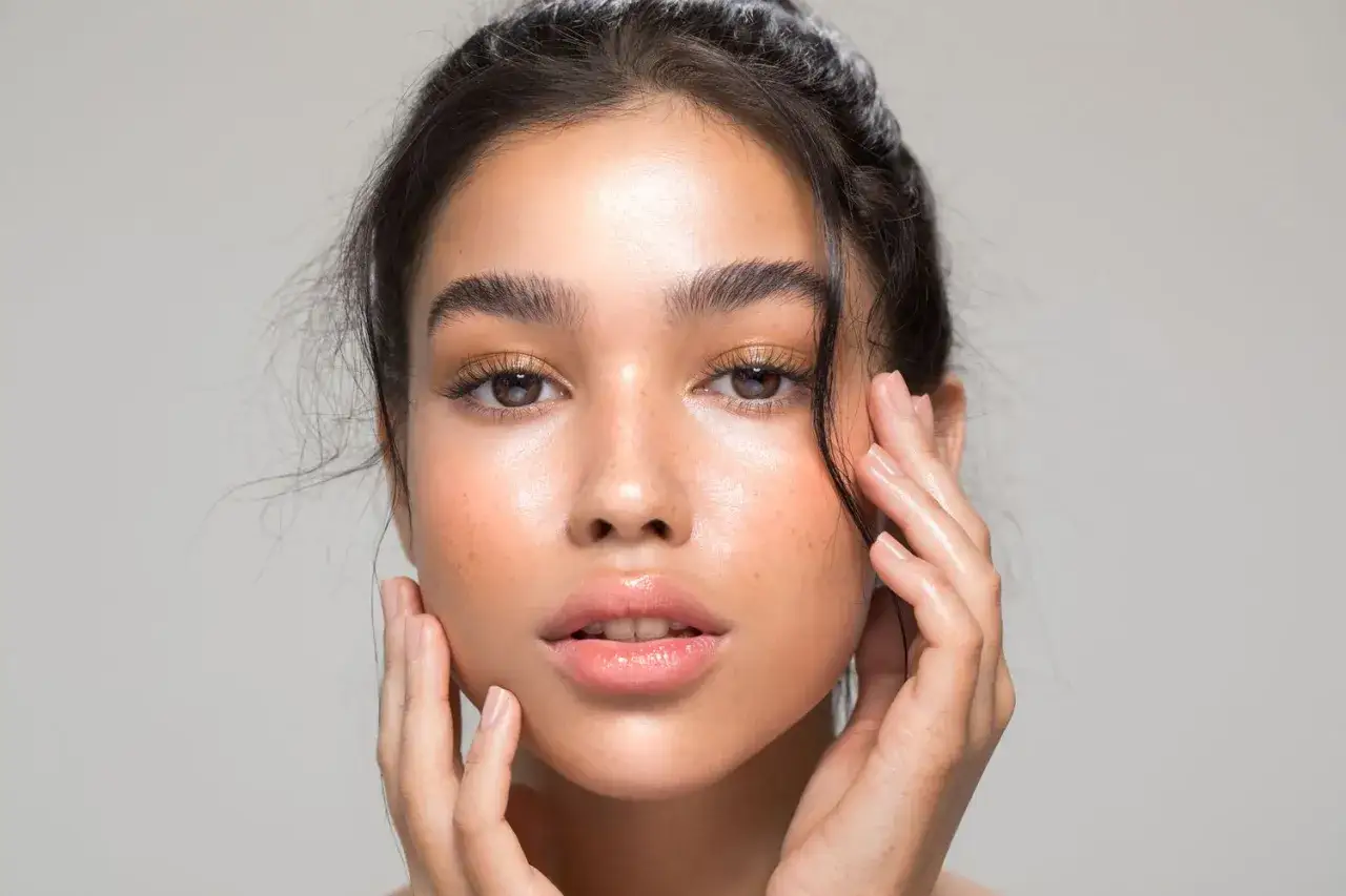 Gesicht einer jungen Frau mit Sommersprossen, die zeigt, wo Highlighter auftragen: auf Wangenknochen und unter den Augenbrauen f&uuml;r einen strahlenden Look.