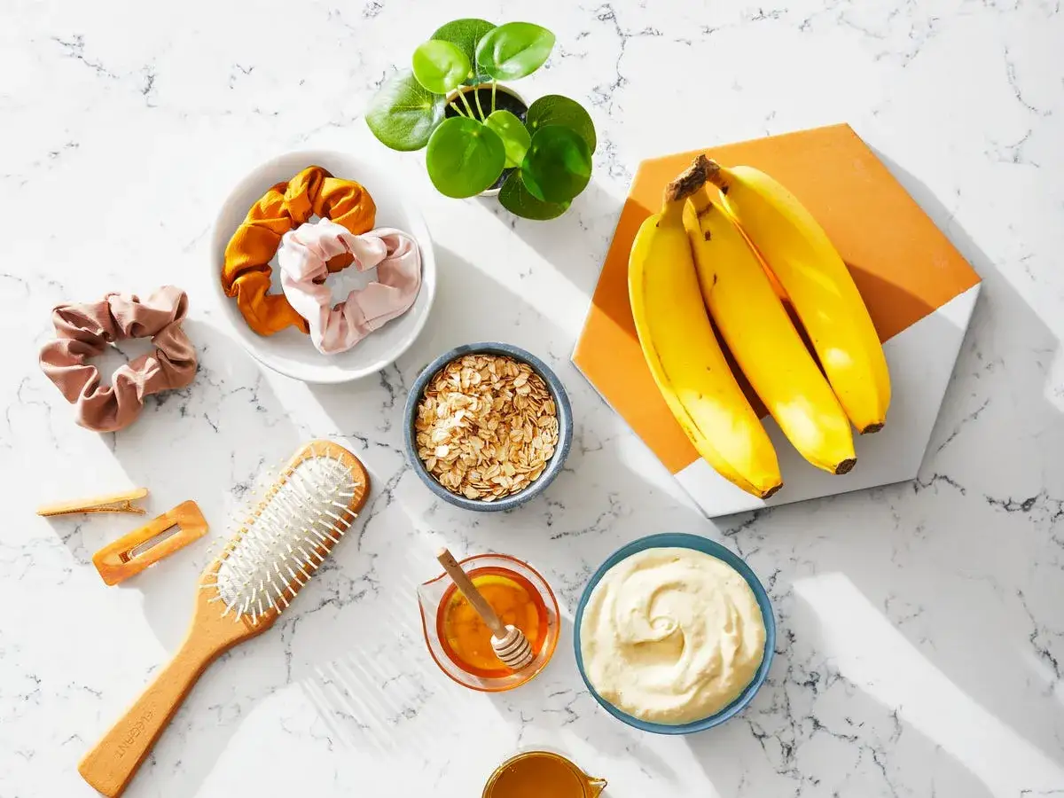 Zutaten für eine Haarkur selber machen: Bananen, Haferflocken, Honig und eine cremige Maske. Dazu Haarbürste und Scrunchies.