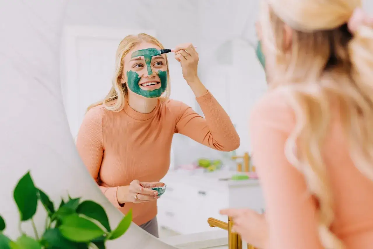 Frau trägt grüne Tonerde Maske auf, um die Wirkung für reine Haut zu erzielen.