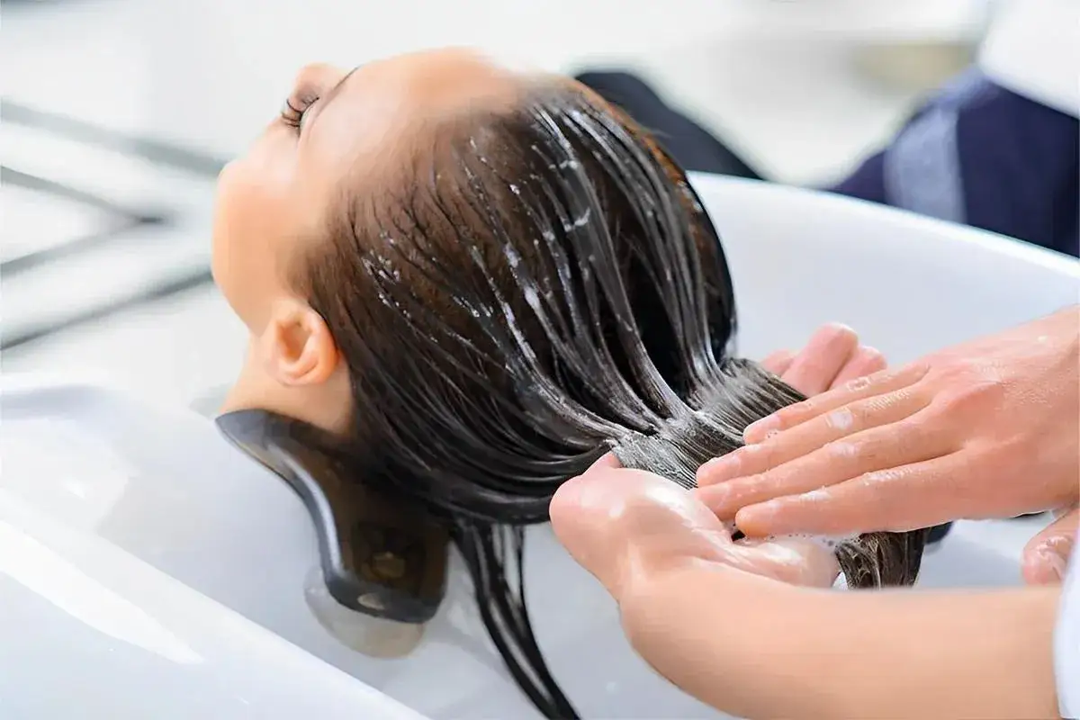 Eine Person erhält eine wohltuende Haar-Conditioner Anwendung im Friseursalon. Hände massieren sanft das nasse Haar.