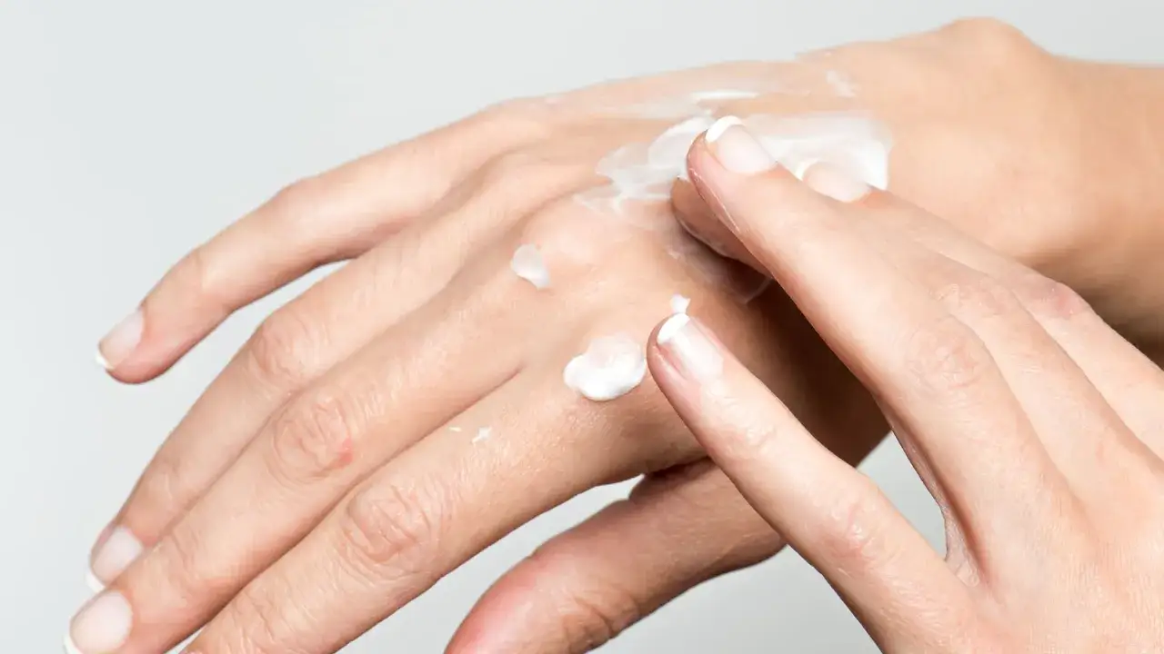 Hände mit trockenen Fingern werden mit weißer Creme eingerieben.