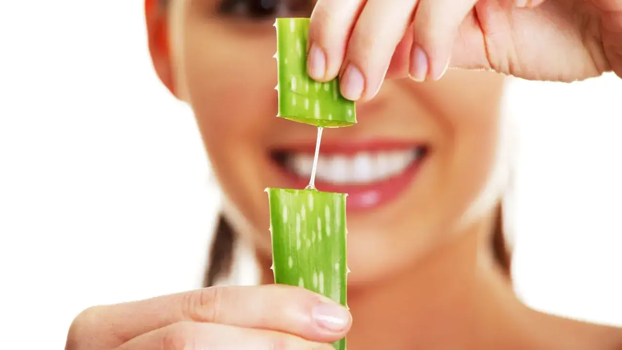 Frau hält Aloe Vera Stücke, aus denen ein Tropfen Gel für die Hautpflege fließt.