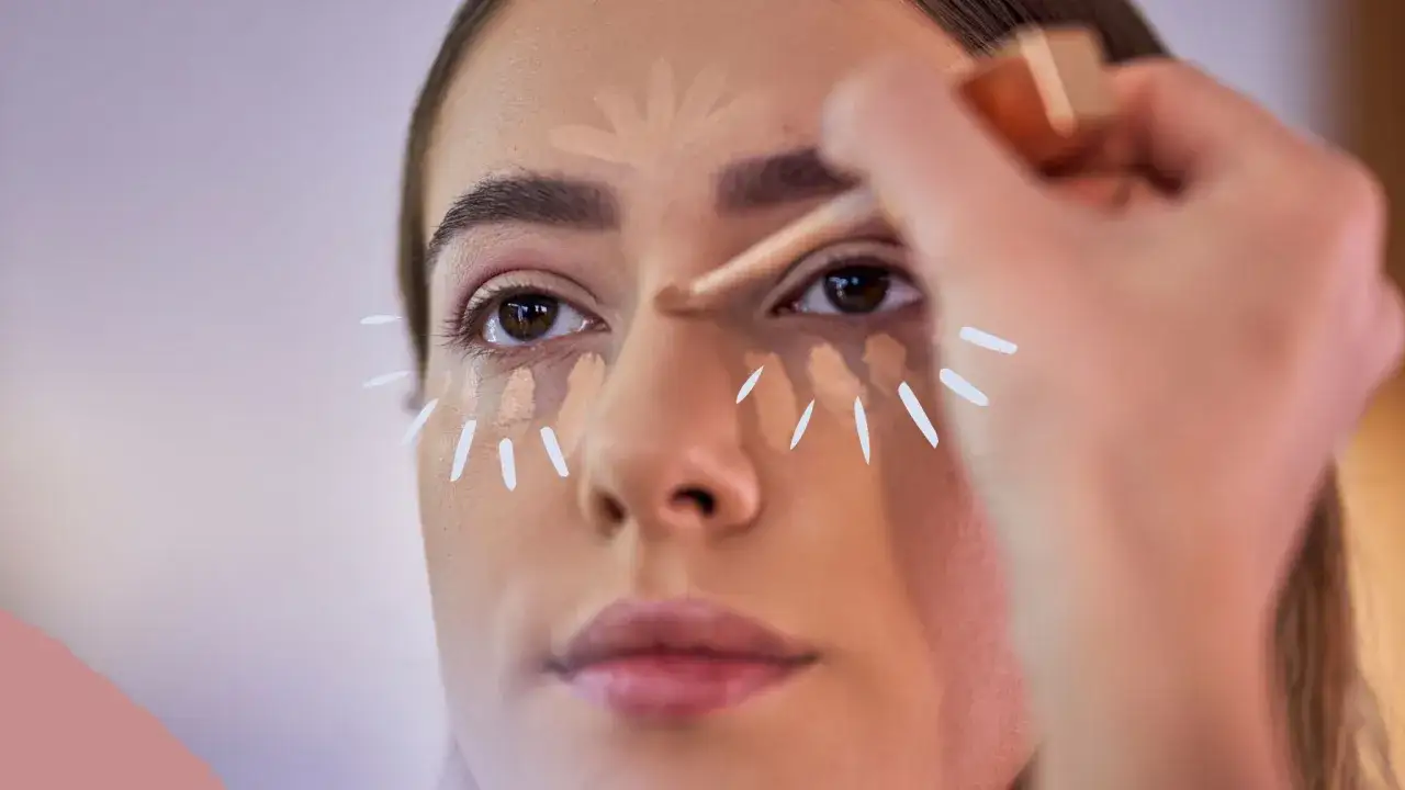 Eine Frau tr&auml;gt Concealer unter den Augen auf, um Augenringe abzudecken. Das zeigt, was ein Concealer ist: ein Produkt zur Hautkorrektur.