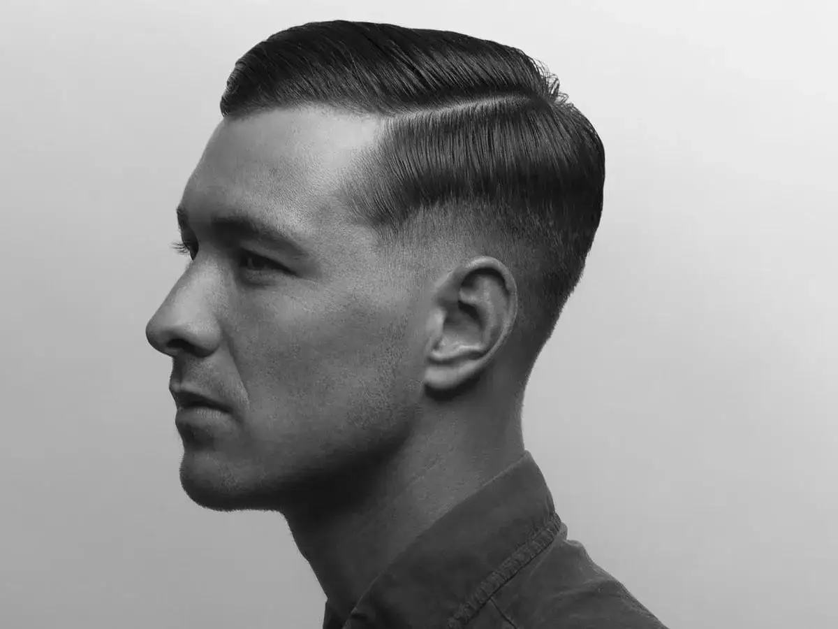 Ein Mann mit einem klassischen Seitenscheitel und einem Fade-Haarschnitt. Die Haare sind glatt und gl&auml;nzend, was zeigt, was ist Pomade: ein Stylingprodukt f&uuml;r perfekten Halt.