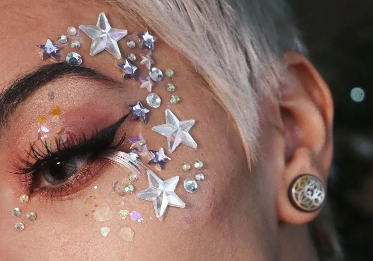 Funkelnder Silvester Make-up Look mit Sternen- und Kristall-Applikationen auf der Wange und am Auge.